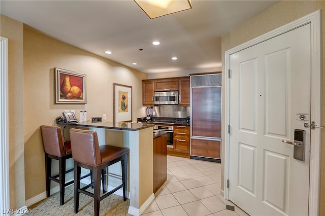 kitchen featuring appliances with stainless steel finishes, kitchen peninsula, a kitchen bar, and light tile patterned floors