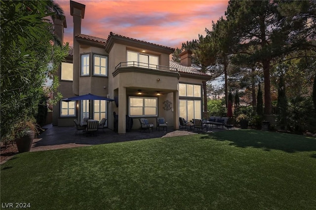 back house at dusk featuring a yard, a balcony, and a patio area