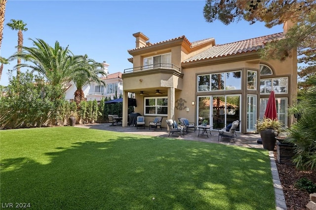 rear view of house with a yard, ceiling fan, a balcony, and a patio