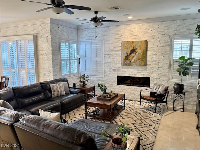 living room featuring a stone fireplace, ceiling fan, tile patterned flooring, and ornamental molding