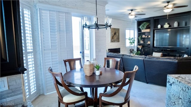 dining room featuring plenty of natural light, a fireplace, and ceiling fan with notable chandelier