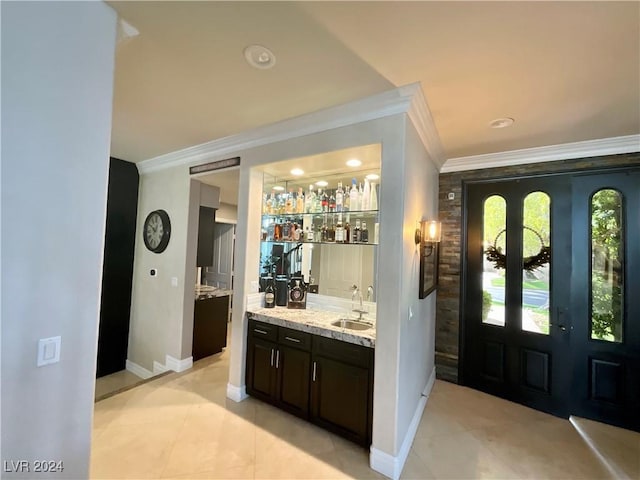 bar with french doors, sink, light stone countertops, ornamental molding, and dark brown cabinetry