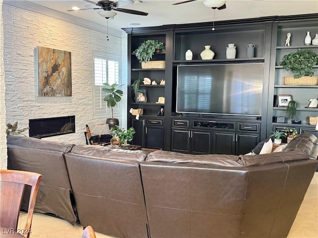 living room with built in shelves, ceiling fan, a stone fireplace, and ornamental molding