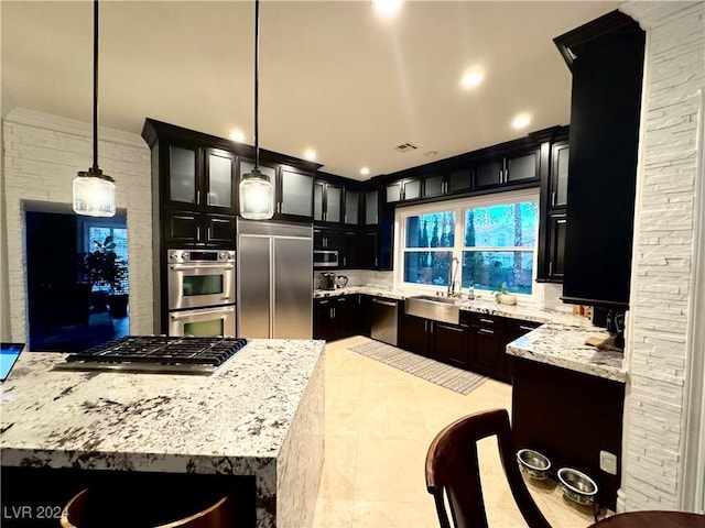 kitchen with light stone countertops, appliances with stainless steel finishes, sink, decorative light fixtures, and a kitchen island