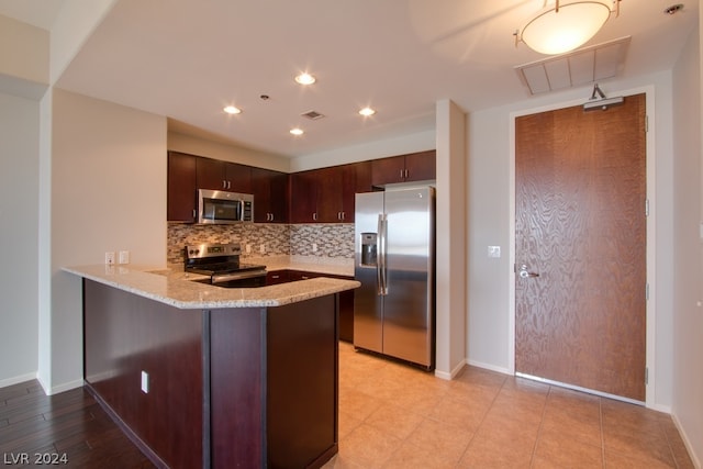 kitchen with stainless steel appliances, light stone countertops, kitchen peninsula, decorative backsplash, and dark brown cabinets