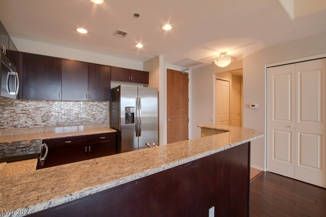 kitchen featuring light stone counters, dark wood-type flooring, stainless steel fridge, decorative backsplash, and dark brown cabinets