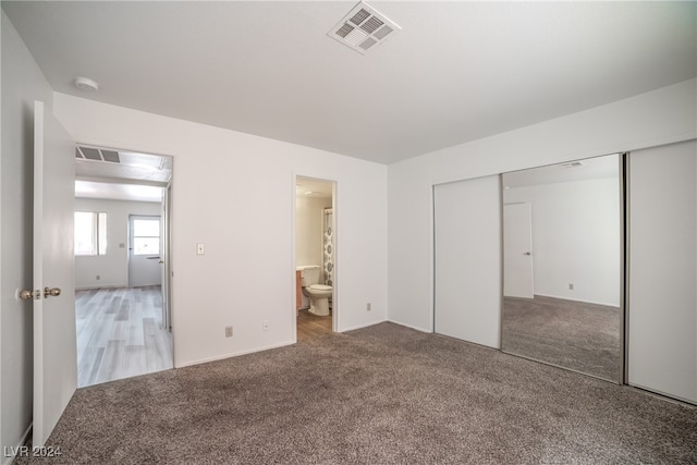 unfurnished bedroom featuring light carpet, a closet, and ensuite bathroom