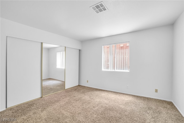 unfurnished bedroom with light colored carpet and a closet