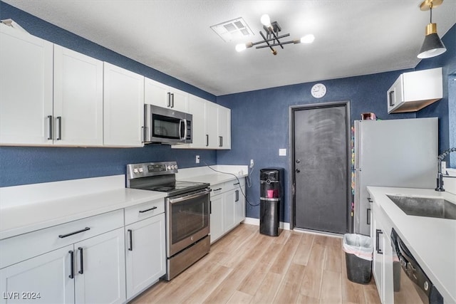 kitchen with light hardwood / wood-style floors, sink, white cabinetry, appliances with stainless steel finishes, and decorative light fixtures