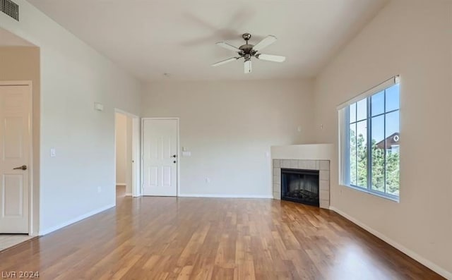 unfurnished living room with wood-type flooring, a tiled fireplace, and ceiling fan