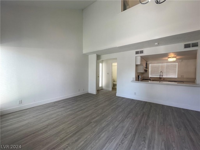 unfurnished living room with dark hardwood / wood-style flooring, sink, and a high ceiling