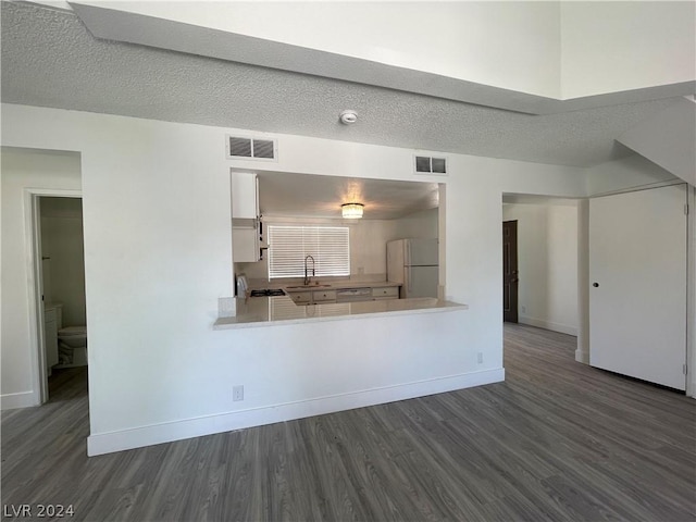 kitchen with dark wood-type flooring, sink, white cabinetry, white refrigerator, and kitchen peninsula