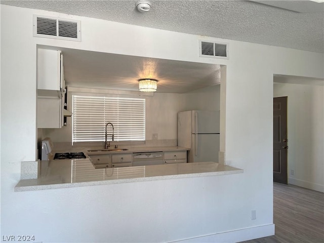 kitchen featuring hardwood / wood-style floors, sink, white cabinets, white appliances, and a textured ceiling