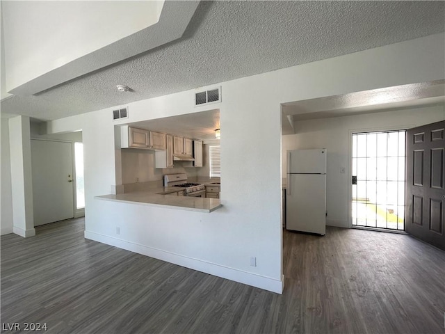 kitchen featuring dark wood-type flooring, light brown cabinetry, a textured ceiling, kitchen peninsula, and white appliances