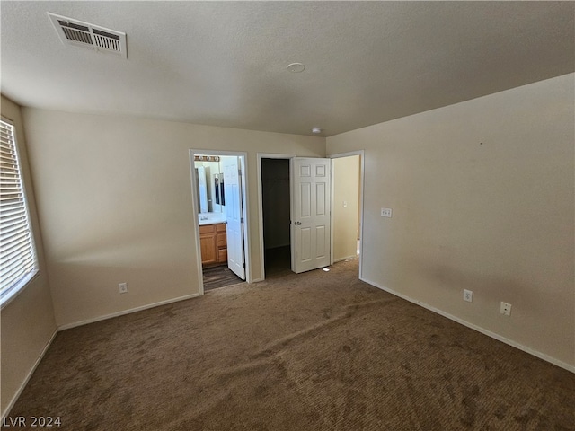 unfurnished bedroom featuring ensuite bath, dark carpet, and a walk in closet