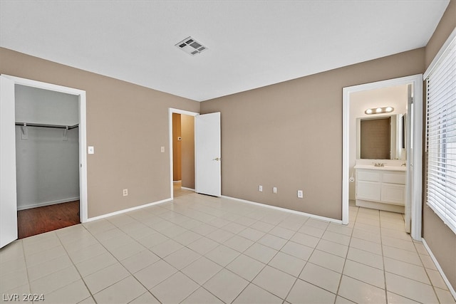 unfurnished bedroom with connected bathroom, a spacious closet, a closet, and light tile patterned flooring