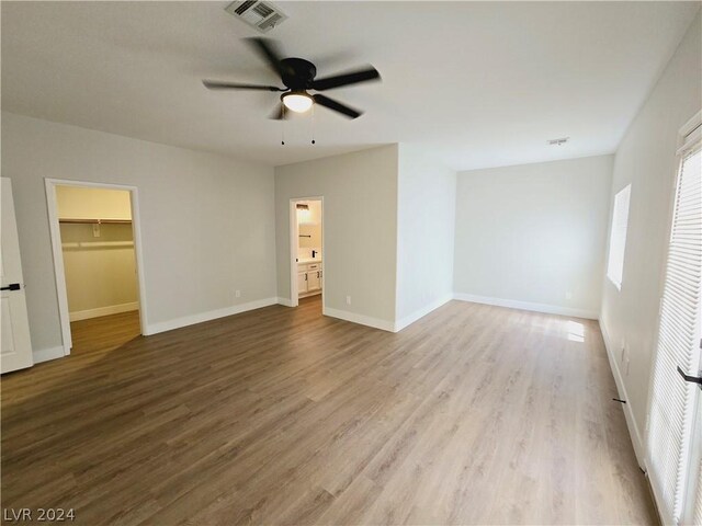 unfurnished bedroom featuring ceiling fan, a walk in closet, and light hardwood / wood-style floors