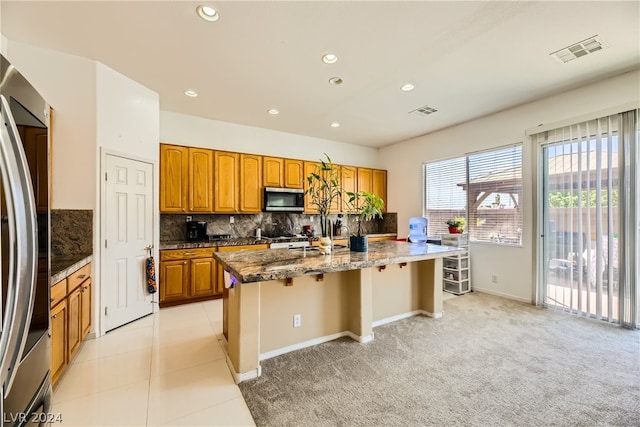 kitchen featuring stainless steel appliances, decorative backsplash, light colored carpet, a center island with sink, and a breakfast bar