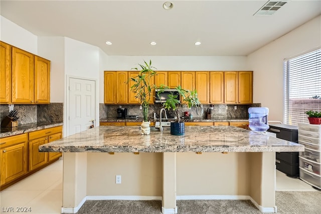 1505 Barrington Oaks St, North Las Vegas, NV 89084 - kitchen featuring light stone countertops, a center island with sink, backsplash, recessed lighting, and brown cabinets