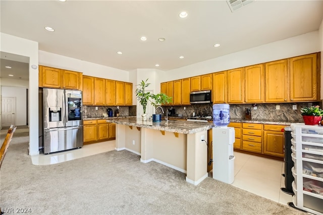 1505 Barrington Oaks St, North Las Vegas, NV 89084 - kitchen featuring appliances with stainless steel finishes, tasteful backsplash, a kitchen island with sink, brown cabinets, and light colored carpet