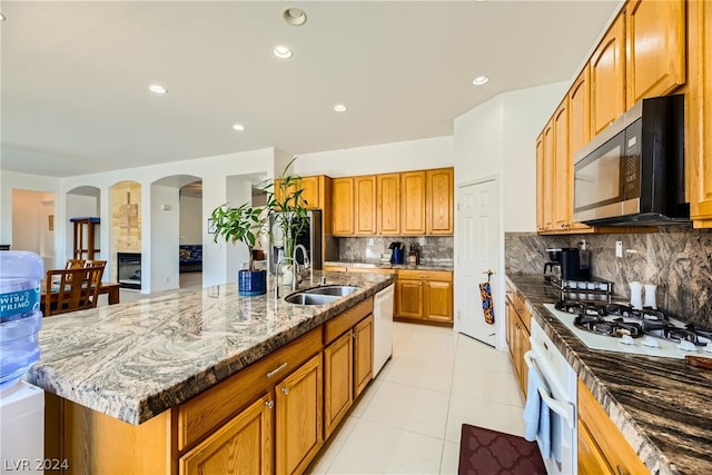 kitchen with tasteful backsplash, wall oven, stone counters, a center island with sink, and light tile patterned floors