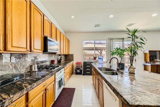 kitchen featuring white appliances, sink, dark stone countertops, light tile patterned floors, and backsplash