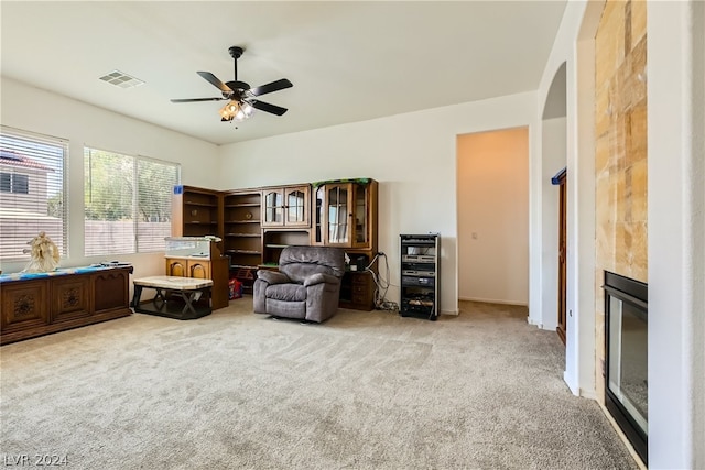 sitting room featuring a fireplace, ceiling fan, and light colored carpet