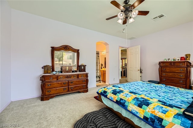 bedroom featuring light carpet, ensuite bathroom, and ceiling fan