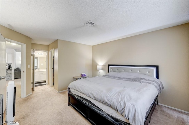 bedroom featuring light colored carpet, a textured ceiling, and ensuite bath