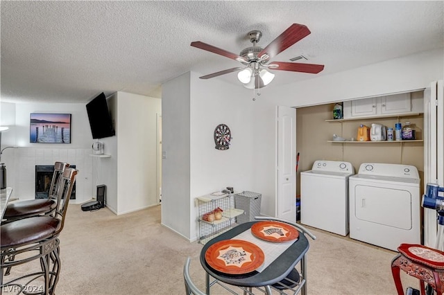 washroom with ceiling fan, a fireplace, washing machine and clothes dryer, a textured ceiling, and light carpet