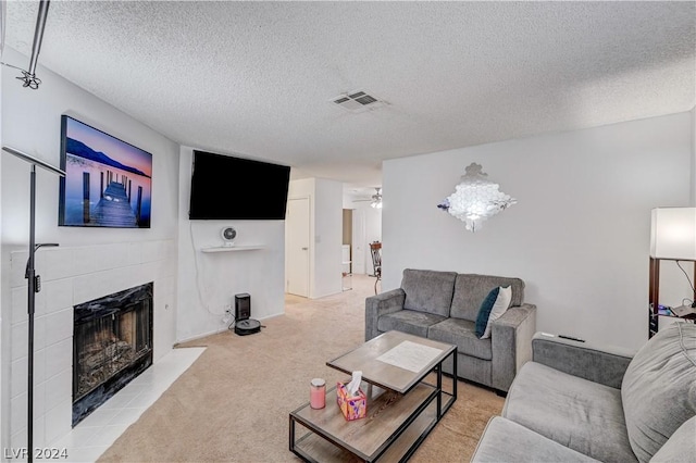 living room with a tile fireplace, light carpet, ceiling fan, and a textured ceiling