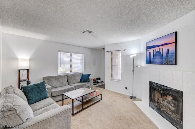 living room with a tile fireplace, light carpet, and a textured ceiling