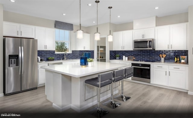 kitchen featuring pendant lighting, light wood-type flooring, tasteful backsplash, white cabinetry, and black appliances