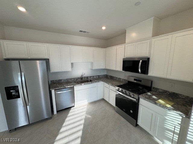 kitchen with white cabinetry, sink, stainless steel appliances, dark stone counters, and light tile patterned floors