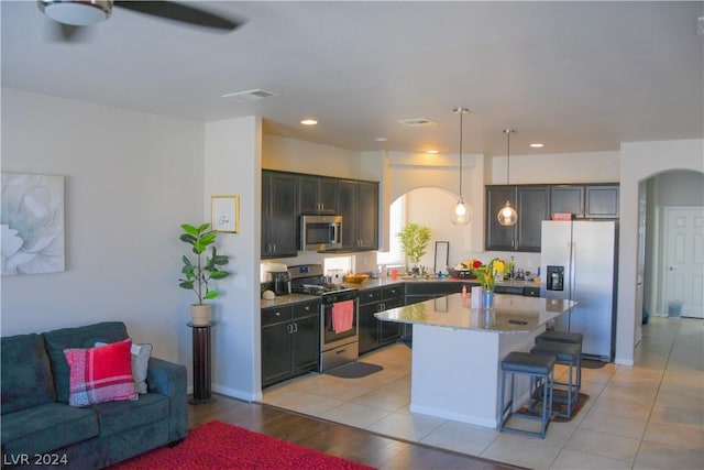 kitchen featuring a breakfast bar, hanging light fixtures, stainless steel appliances, light stone counters, and a kitchen island