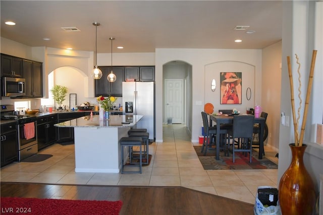 kitchen featuring hanging light fixtures, a center island, light tile patterned floors, light stone counters, and stainless steel appliances