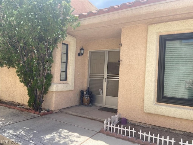 view of exterior entry featuring a patio, fence, and stucco siding