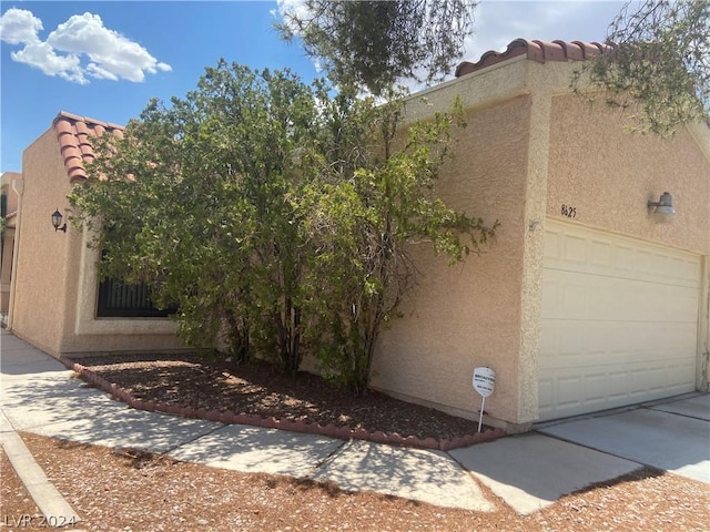 view of side of property with stucco siding, a garage, and a tiled roof