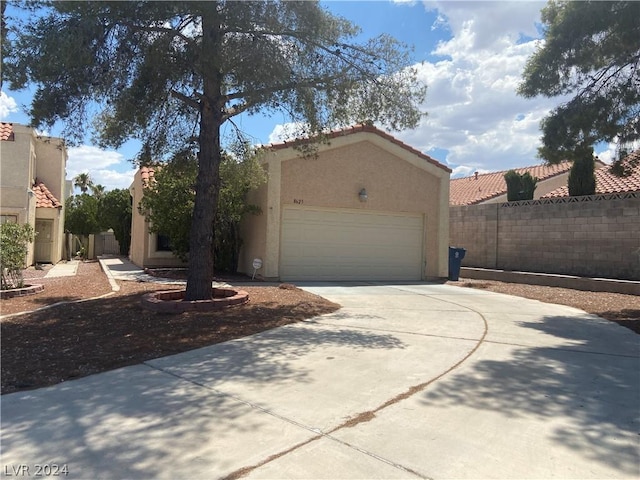 view of front facade with stucco siding, a tile roof, concrete driveway, and fence