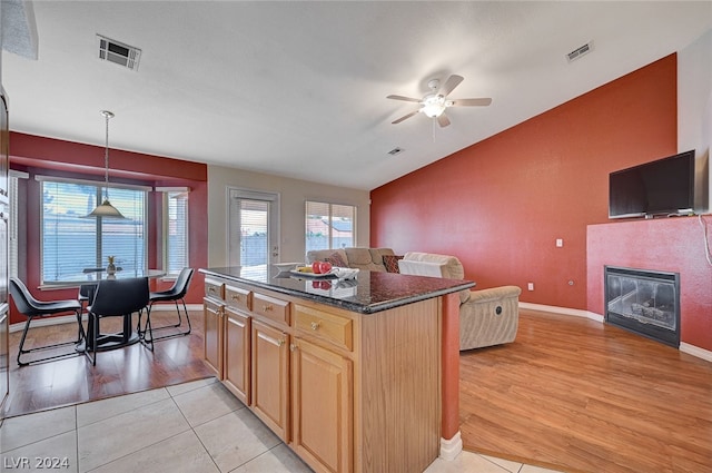 kitchen with dark stone counters, light hardwood / wood-style flooring, a kitchen island, lofted ceiling, and ceiling fan