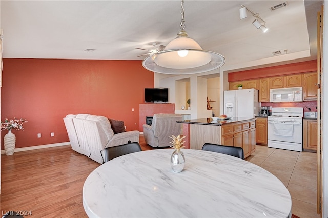 dining space featuring lofted ceiling, rail lighting, light tile patterned floors, ceiling fan, and a raised ceiling