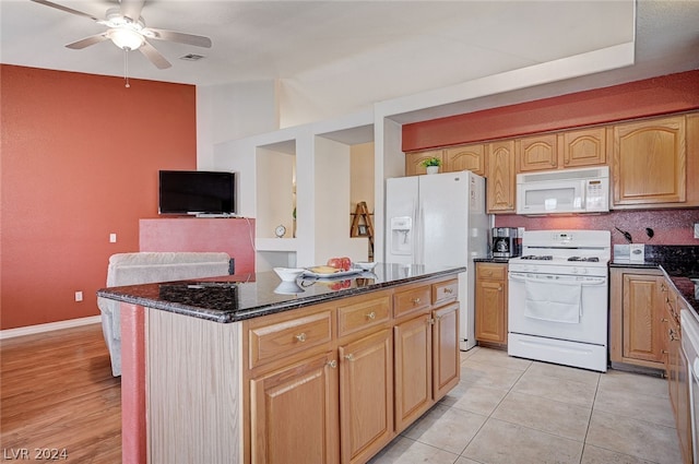 kitchen featuring white appliances, light wood-type flooring, dark stone counters, a kitchen island, and ceiling fan