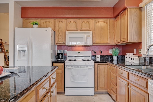 kitchen with light brown cabinets, light tile patterned floors, white appliances, dark stone counters, and sink