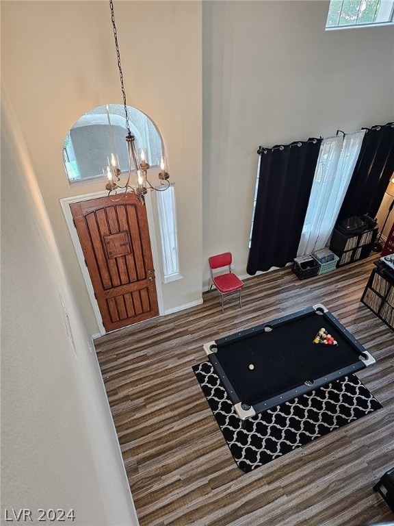 entryway with billiards, a towering ceiling, wood-type flooring, and a chandelier