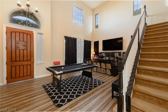 game room featuring a towering ceiling, a notable chandelier, pool table, and light wood-type flooring