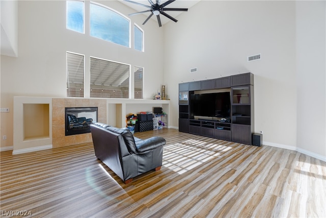 living room featuring a tile fireplace, ceiling fan, hardwood / wood-style flooring, and a towering ceiling