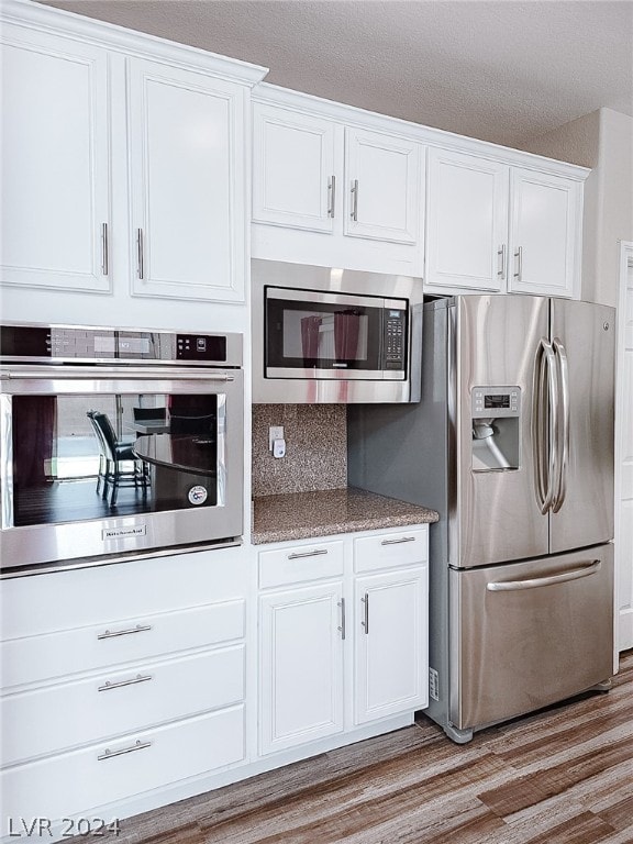 kitchen featuring stone counters, stainless steel appliances, white cabinets, light hardwood / wood-style floors, and decorative backsplash