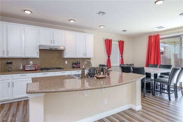 kitchen featuring a center island with sink, tasteful backsplash, sink, and light wood-type flooring