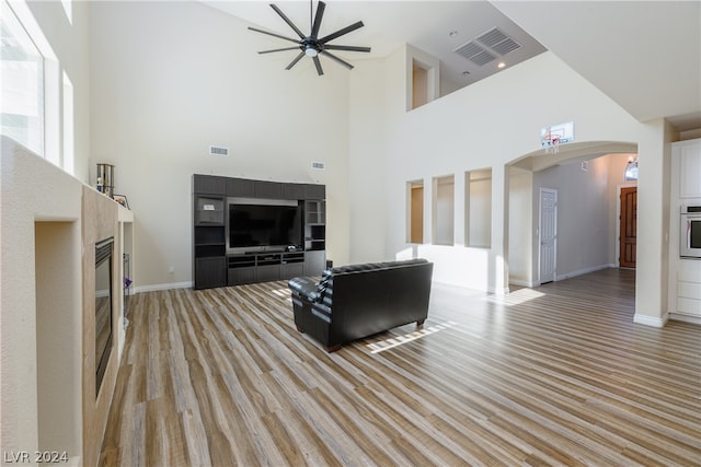 living room with light wood-type flooring, ceiling fan, and a towering ceiling