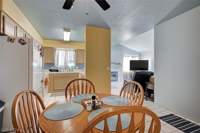 dining space featuring sink, a tiled fireplace, vaulted ceiling, light tile patterned floors, and ceiling fan